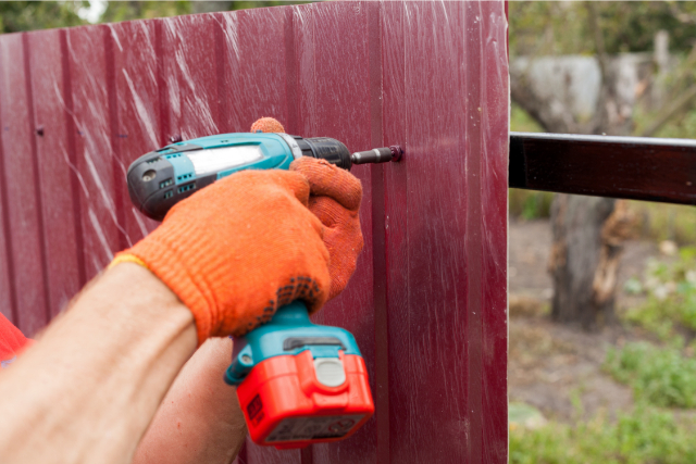 Metal fence installation by worker in gloves with a drill